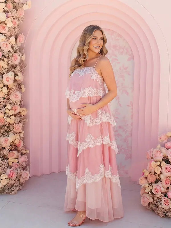 A pink tiered lace maternity maxi dress with layered chiffon, white lace trim, and an adjustable lace-up back for baby shower, maternity photoshoot, gender reveal, and bridal shower.
