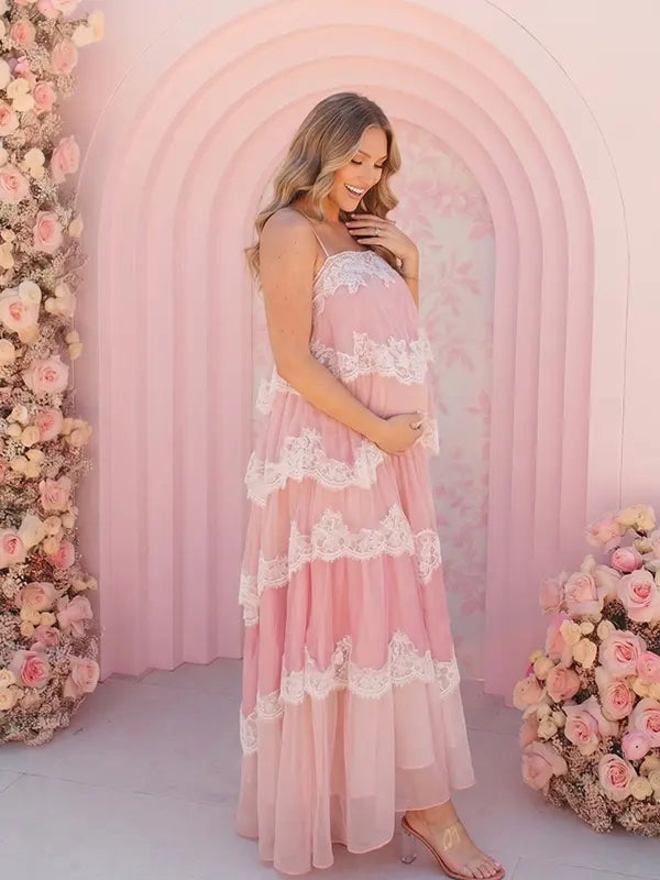 A pink tiered lace maternity maxi dress with layered chiffon, white lace trim, and an adjustable lace-up back for baby shower, maternity photoshoot, gender reveal, and bridal shower.