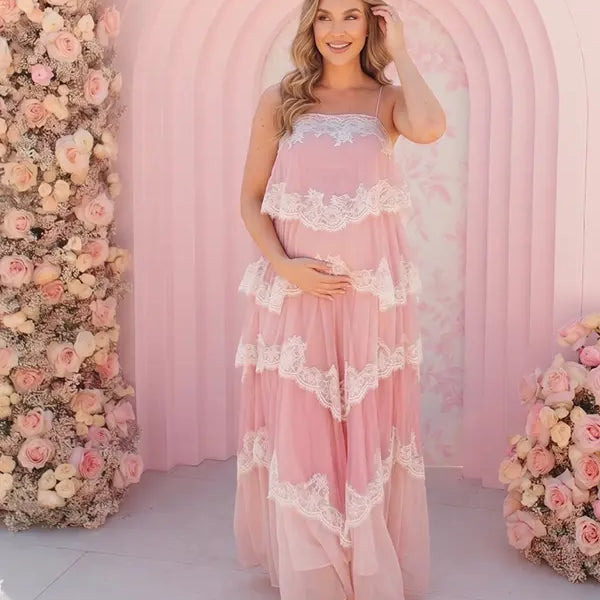 A pink tiered lace maternity maxi dress with layered chiffon, white lace trim, and an adjustable lace-up back for baby shower, maternity photoshoot, gender reveal, and bridal shower.