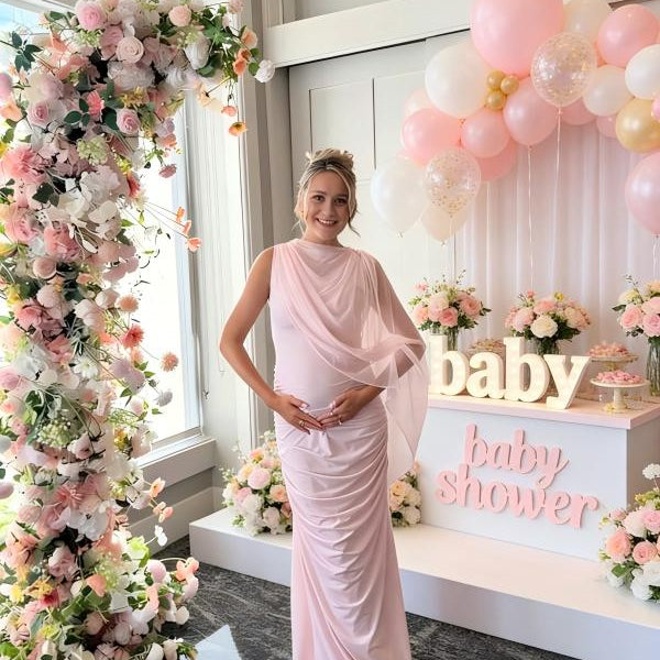 Pregnant woman wearing blush pink one shoulder draped maternity maxi dress for baby shower photoshoot