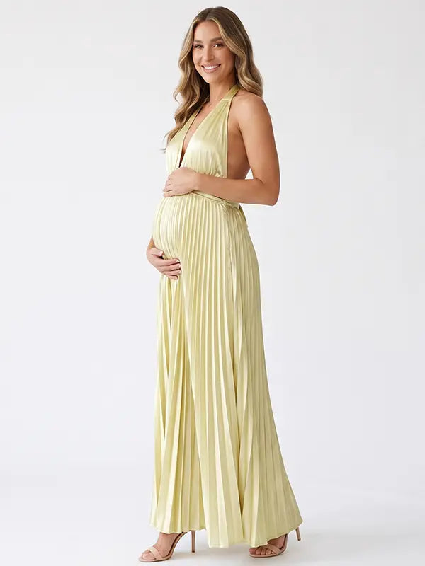 Pregnant model wearing a butter yellow pleated satin halter maternity maxi dress with deep V neckline and flowing skirt for summer baby shower, garden party and maternity photoshoot.