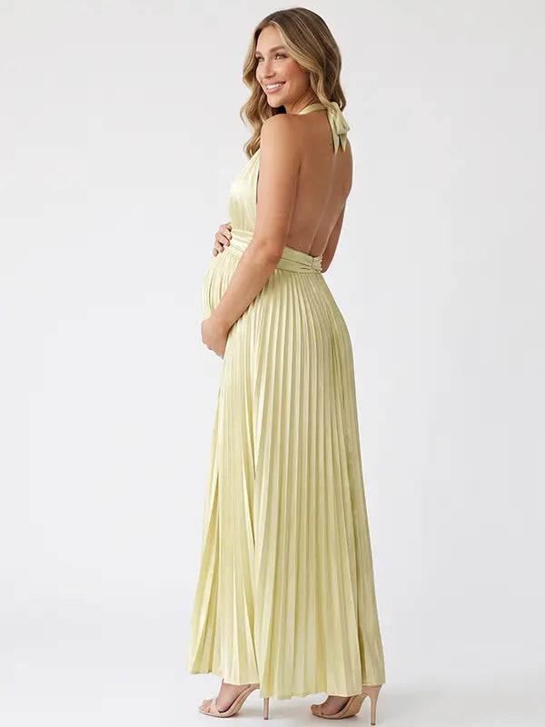 Pregnant model wearing a butter yellow pleated satin halter maternity maxi dress with deep V neckline and flowing skirt for summer baby shower, garden party and maternity photoshoot.