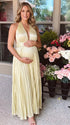 Pregnant model wearing a butter yellow pleated satin halter maternity maxi dress with deep V neckline and flowing skirt for summer baby shower, garden party and maternity photoshoot.