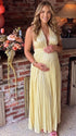 Pregnant model wearing a butter yellow pleated satin halter maternity maxi dress with deep V neckline and flowing skirt for summer baby shower, garden party and maternity photoshoot.