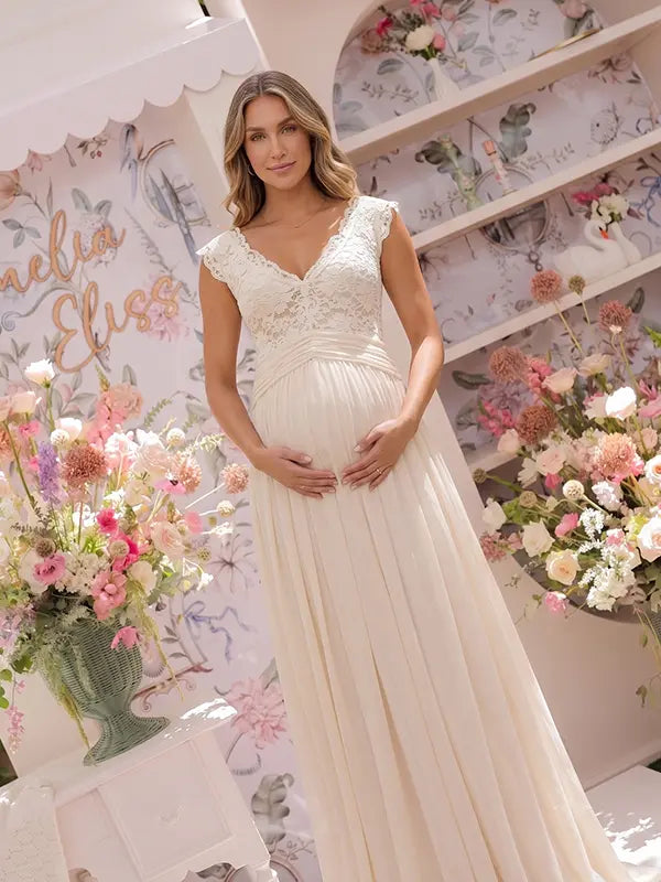 An ivory lace chiffon maternity maxi dress with floral lace bodice, flutter sleeves and flowing skirt for boho baby shower, maternity photoshoot and bridal celebration.