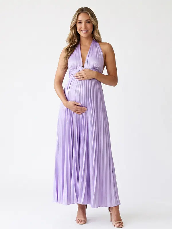 Pregnant model wearing a lavender pleated satin halter maternity maxi dress with deep V neckline and flowing skirt for spring baby shower, garden party and maternity photoshoot.
