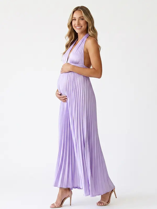 Pregnant model wearing a lavender pleated satin halter maternity maxi dress with deep V neckline and flowing skirt for spring baby shower, garden party and maternity photoshoot.