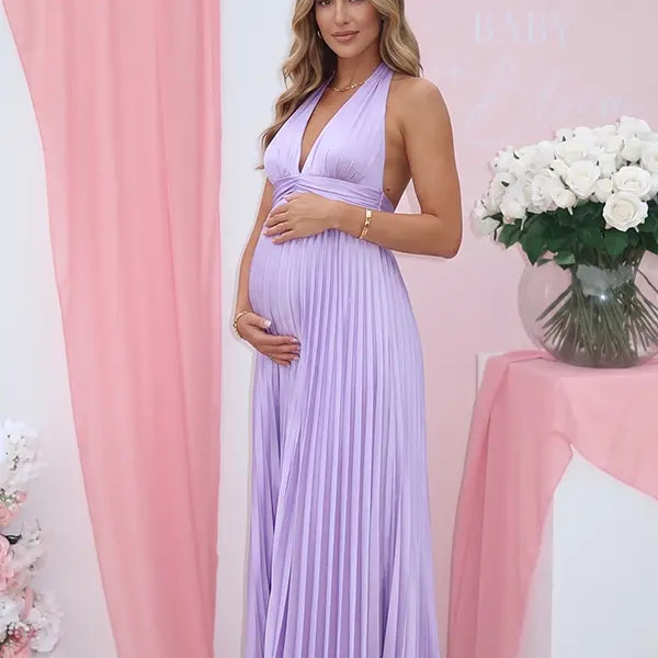 Pregnant model wearing a lavender pleated satin halter maternity maxi dress with deep V neckline and flowing skirt for spring baby shower, garden party and maternity photoshoot.