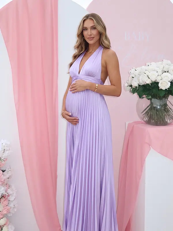 Pregnant model wearing a lavender pleated satin halter maternity maxi dress with deep V neckline and flowing skirt for spring baby shower, garden party and maternity photoshoot.