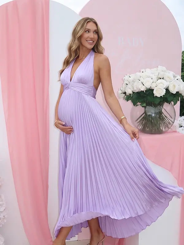 Pregnant model wearing a lavender pleated satin halter maternity maxi dress with deep V neckline and flowing skirt for spring baby shower, garden party and maternity photoshoot.