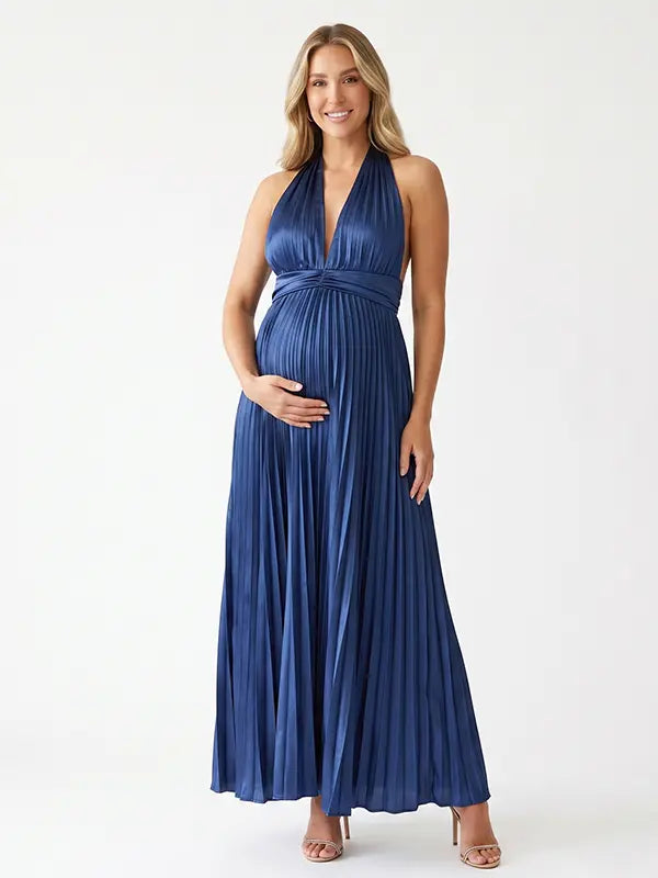 Pregnant model wearing a navy blue pleated satin halter maternity maxi dress with deep V neckline and flowing skirt for wedding guest, maternity photoshoot and formal occasions.