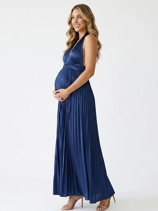 Pregnant model wearing a navy blue pleated satin halter maternity maxi dress with deep V neckline and flowing skirt for wedding guest, maternity photoshoot and formal occasions.