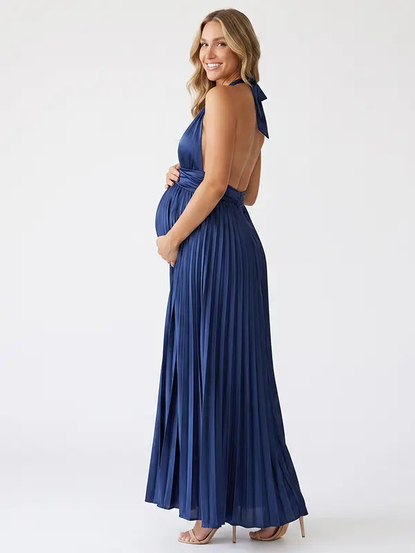 Pregnant model wearing a navy blue pleated satin halter maternity maxi dress with deep V neckline and flowing skirt for wedding guest, maternity photoshoot and formal occasions.