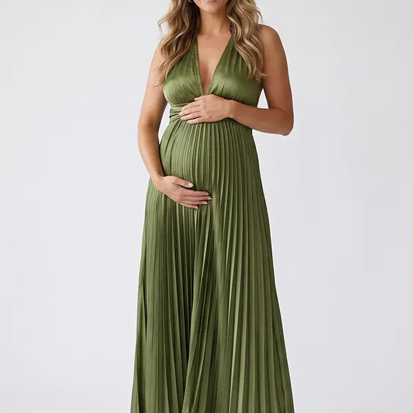 Pregnant model wearing an olive green pleated satin halter maternity maxi dress with deep V neckline and flowing skirt for boho baby shower, rustic maternity photoshoot and outdoor pregnancy celebration.