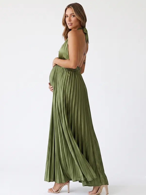 Pregnant model wearing an olive green pleated satin halter maternity maxi dress with deep V neckline and flowing skirt for boho baby shower, rustic maternity photoshoot and outdoor pregnancy celebration.