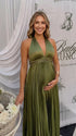 Pregnant model wearing an olive green pleated satin halter maternity maxi dress with deep V neckline and flowing skirt for boho baby shower, rustic maternity photoshoot and outdoor pregnancy celebration.