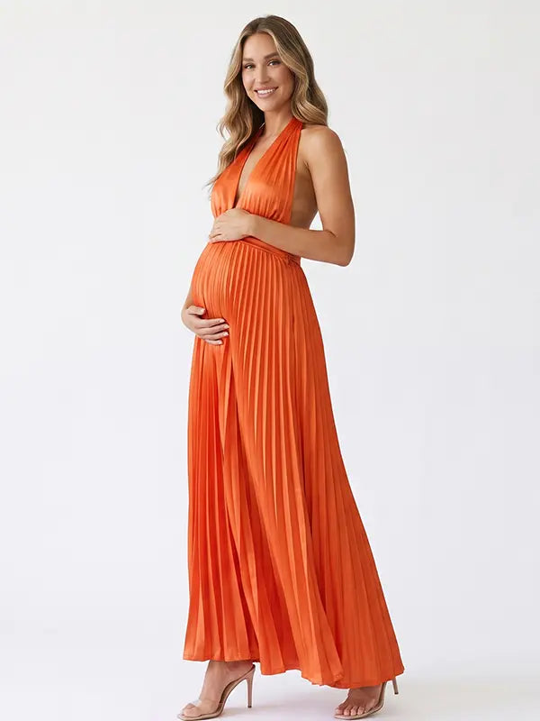 Pregnant model wearing an orange pleated satin halter maternity maxi dress with deep V neckline and flowing skirt for fall baby shower, pumpkin patch photos and maternity photography.