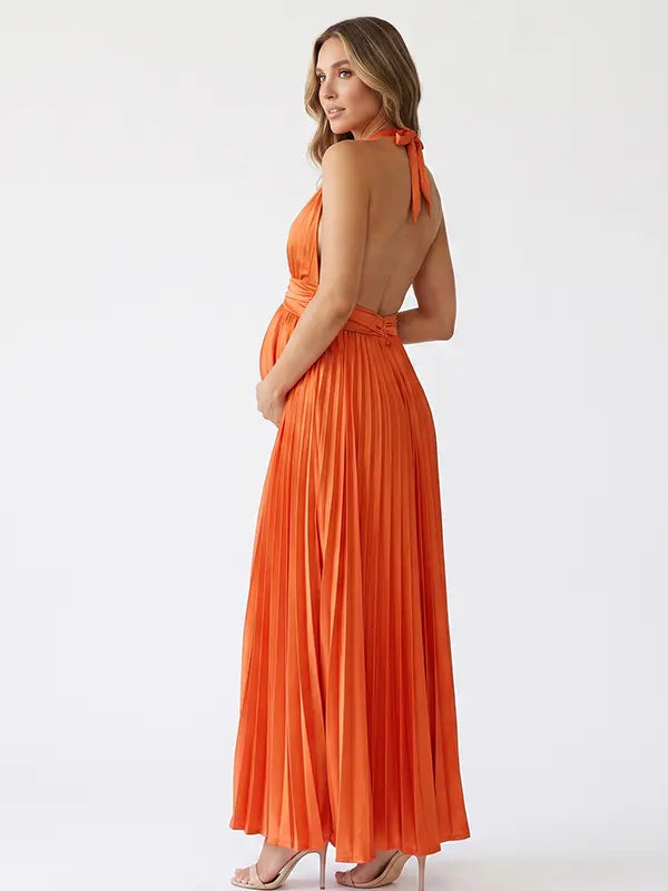 Pregnant model wearing an orange pleated satin halter maternity maxi dress with deep V neckline and flowing skirt for fall baby shower, pumpkin patch photos and maternity photography.