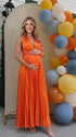 Pregnant model wearing an orange pleated satin halter maternity maxi dress with deep V neckline and flowing skirt for fall baby shower, pumpkin patch photos and maternity photography.
