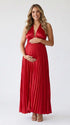 Pregnant model wearing a red pleated satin halter maternity maxi dress with deep V neckline, empire waist and flowing skirt for baby shower, gender reveal and maternity photoshoot.