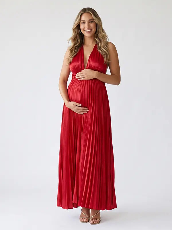 Pregnant model wearing a red pleated satin halter maternity maxi dress with deep V neckline, empire waist and flowing skirt for baby shower, gender reveal and maternity photoshoot.