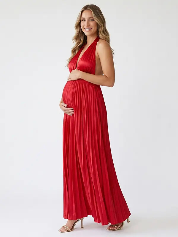 Pregnant model wearing a red pleated satin halter maternity maxi dress with deep V neckline, empire waist and flowing skirt for baby shower, gender reveal and maternity photoshoot.