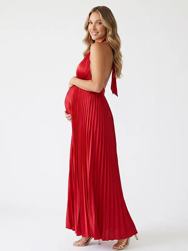 Pregnant model wearing a red pleated satin halter maternity maxi dress with deep V neckline, empire waist and flowing skirt for baby shower, gender reveal and maternity photoshoot.