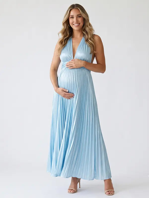 Pregnant model wearing a sky blue pleated satin halter maternity maxi dress with deep V neckline and flowing skirt for beach maternity photoshoot, coastal baby shower and destination pregnancy photography.