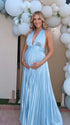 Pregnant model wearing a sky blue pleated satin halter maternity maxi dress with deep V neckline and flowing skirt for beach maternity photoshoot, coastal baby shower and destination pregnancy photography.