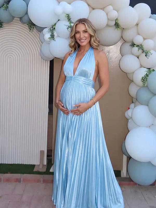 Pregnant model wearing a sky blue pleated satin halter maternity maxi dress with deep V neckline and flowing skirt for beach maternity photoshoot, coastal baby shower and destination pregnancy photography.