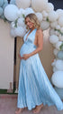 Pregnant model wearing a sky blue pleated satin halter maternity maxi dress with deep V neckline and flowing skirt for beach maternity photoshoot, coastal baby shower and destination pregnancy photography.