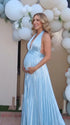 Pregnant model wearing a sky blue pleated satin halter maternity maxi dress with deep V neckline and flowing skirt for beach maternity photoshoot, coastal baby shower and destination pregnancy photography.