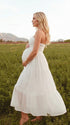 A smiling pregnant woman wearing a yellow tiered halter-neck maternity midi dress. The dress features a smocked bust and flowy skirt, ideal for a summer baby shower or outdoor photoshoot.